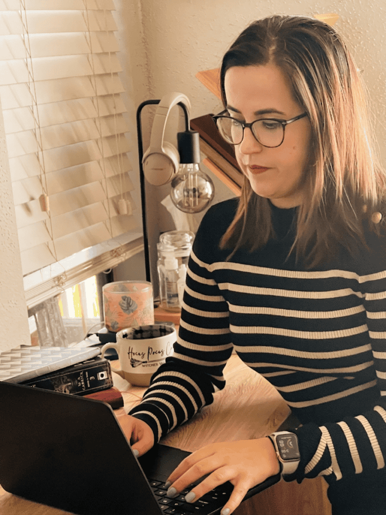 Professional beta readder Daniella Linares sitting at a wood desk, working on her laptop