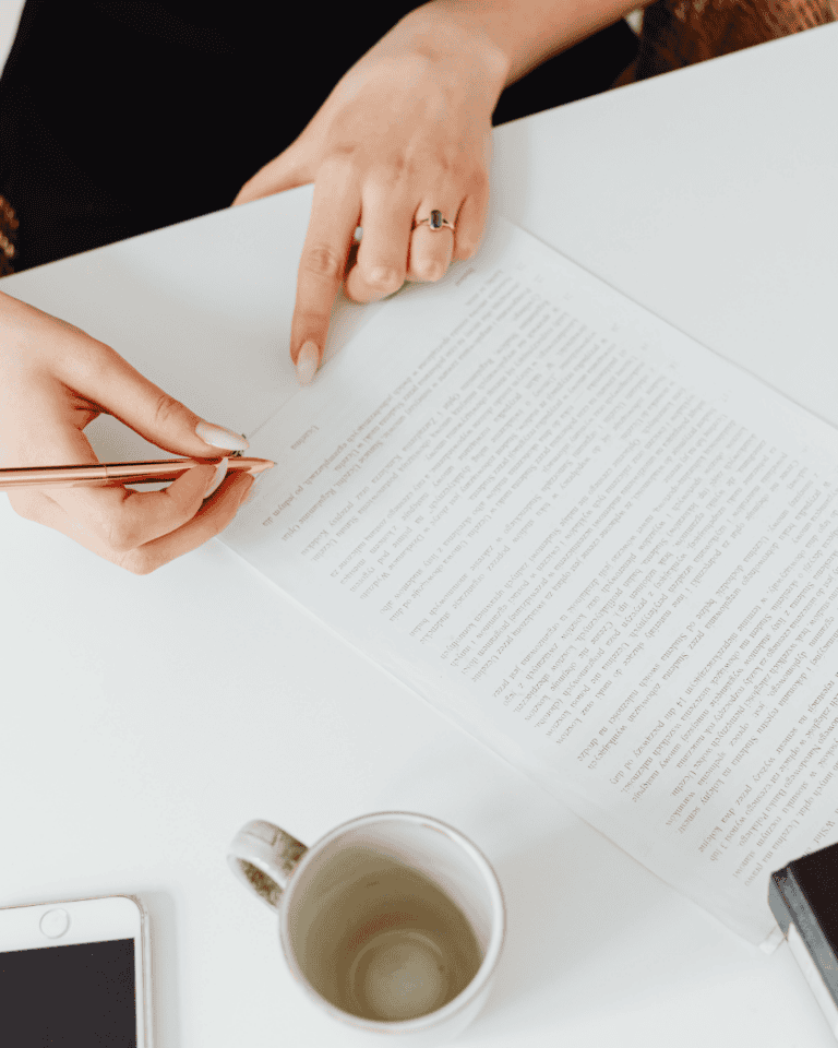 A reader reviewing a printed manuscript with a pen in hand, pointing to a specific passage, the close, attentive reading that produces detailed beta reading feedback authors can act on.