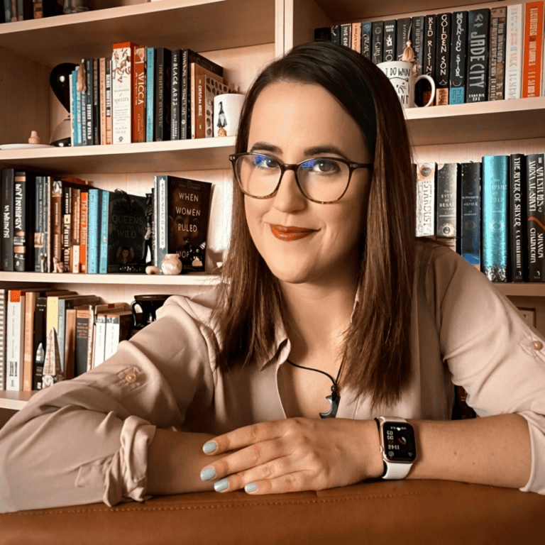 Daniella Marie, published writer and professional beta reader, at her desk surrounded by fantasy, historical fiction, and literary titles.