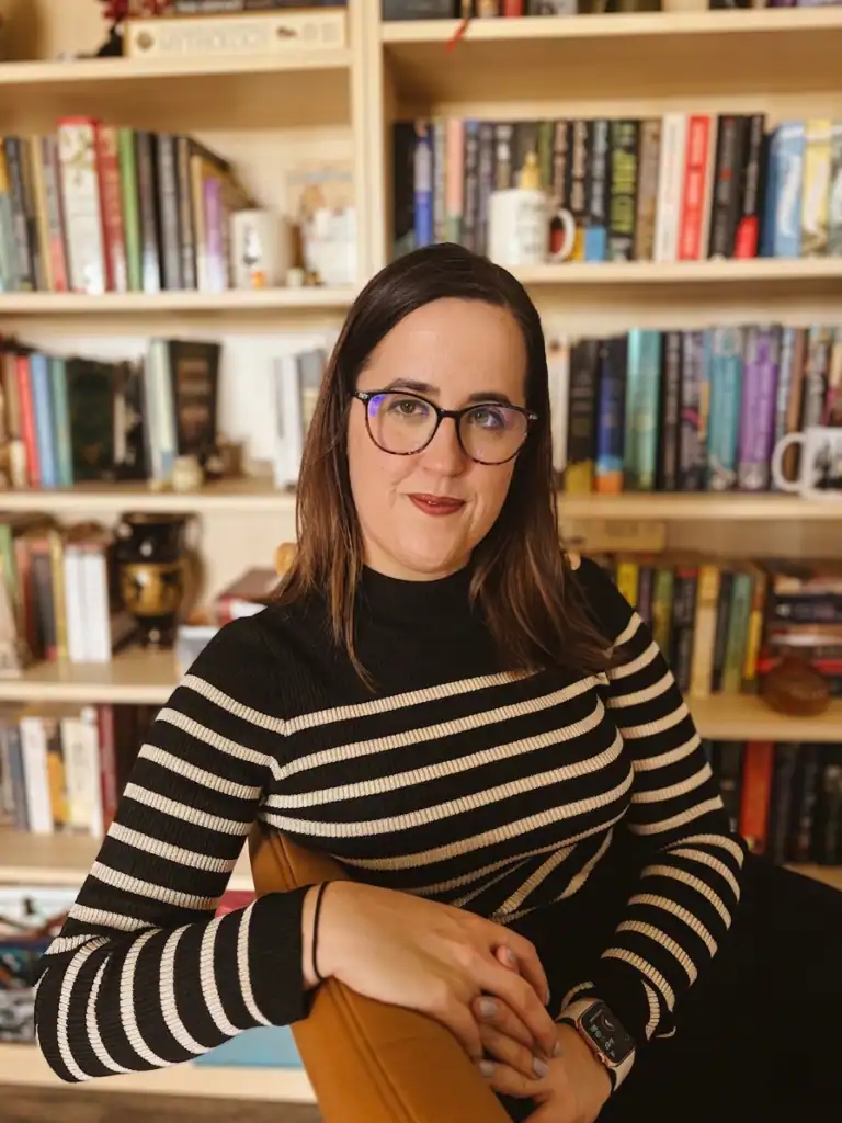 Daniella Marie, professional beta reading specialist, seated in front of her home library of fiction, fantasy, and memoir titles she draws on for craft-driven manuscript feedback.
